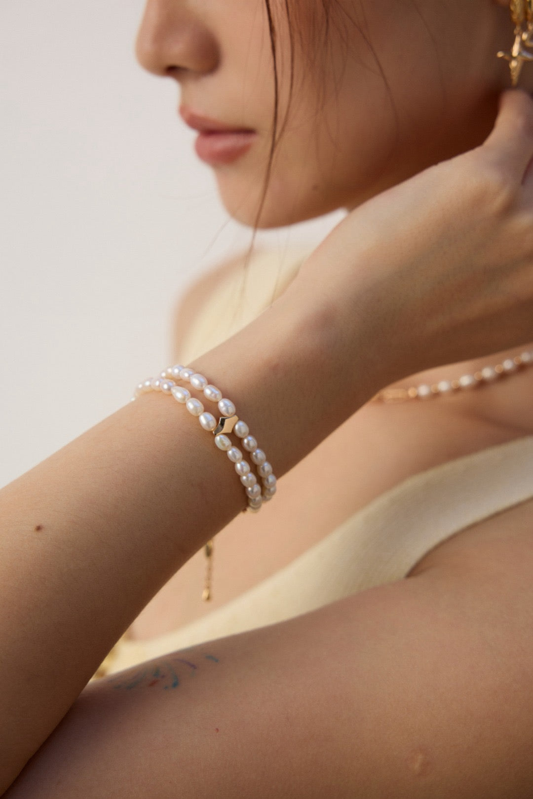 Lifestyle view of a model's arm highlighting the delicate profile of the Andie double-strand freshwater pearl bracelet, paired with a subtle gold extension chain.