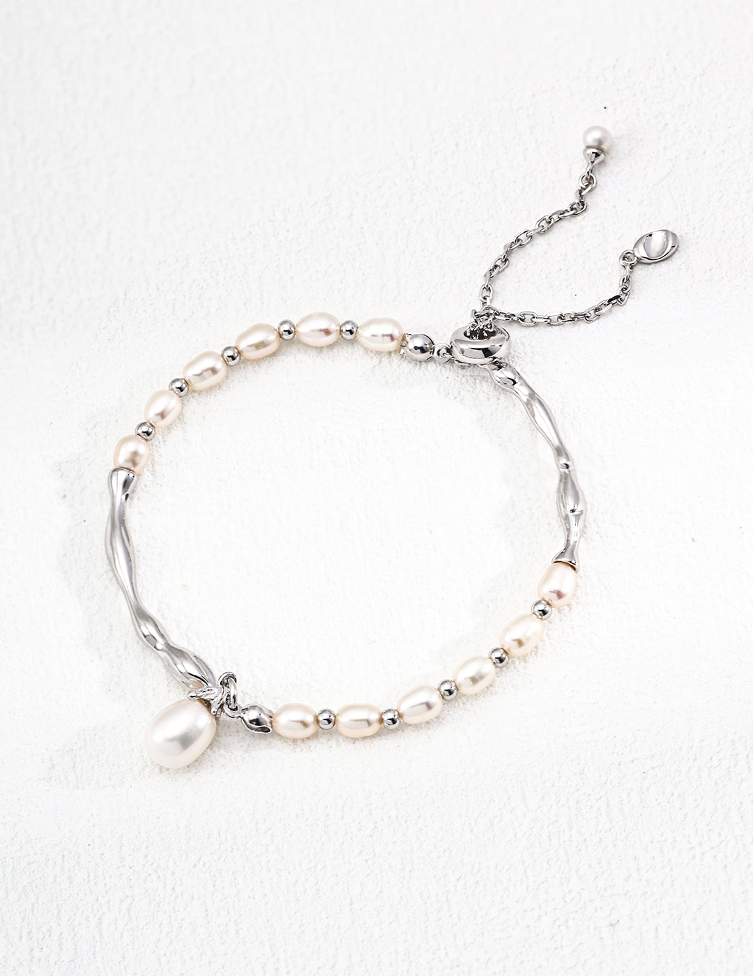 A delicate bracelet featuring small, cream-colored pearls intertwined with twisted silver links, finished with a simple chain clasp on a light surface.