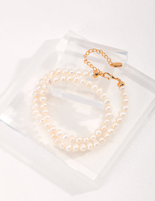 A delicate white pearl bracelet displayed on a transparent surface, enhancing the allure of an elegant freshwater pearl necklace.