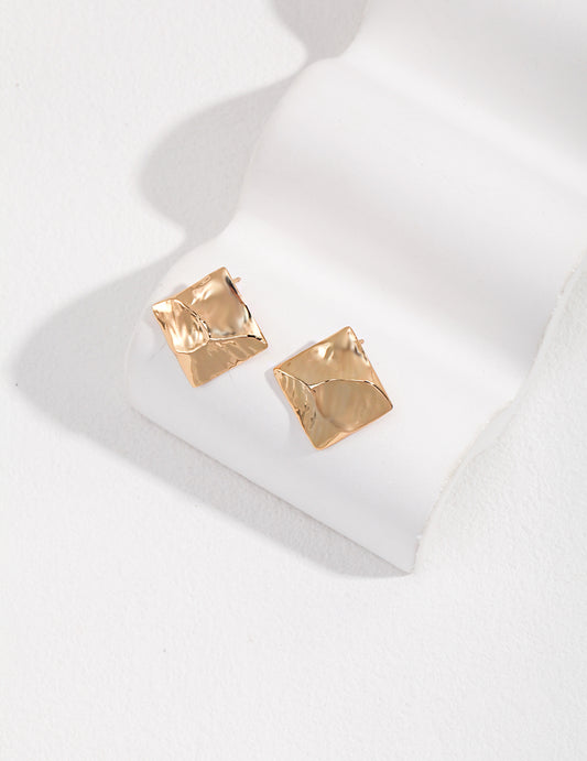 Gold square stud earrings on white surface.