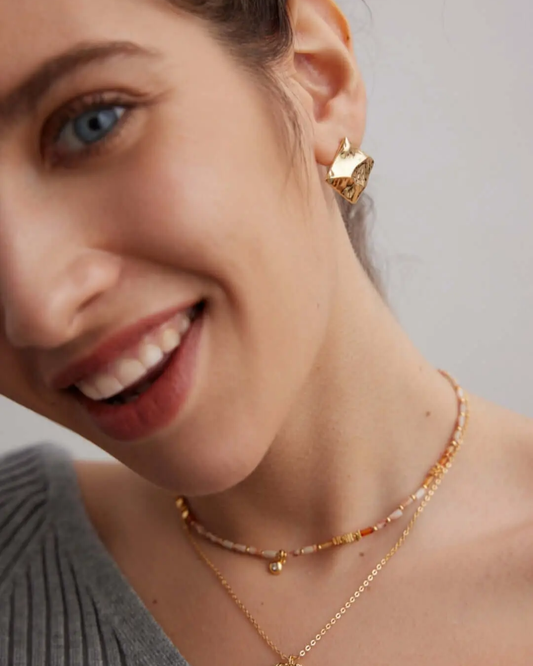 A woman adorned with a colorful gemstone necklace and gold earrings, highlighting her fashionable and vibrant look.