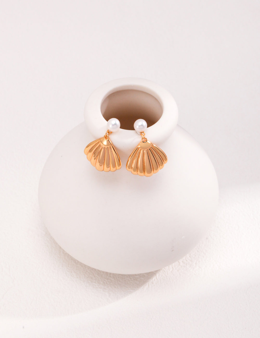 A stylish white vase holds a stunning pair of gold earrings, highlighting their luxurious design against a simple backdrop.