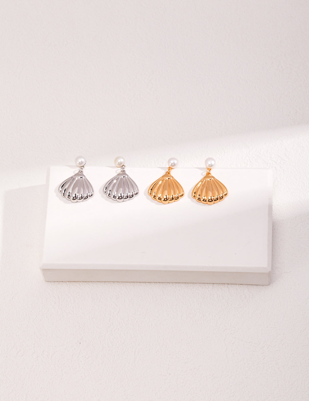 A white box displays two pairs of earrings distinct shells in vibrant colors, accented with silver and gold details for added elegance.