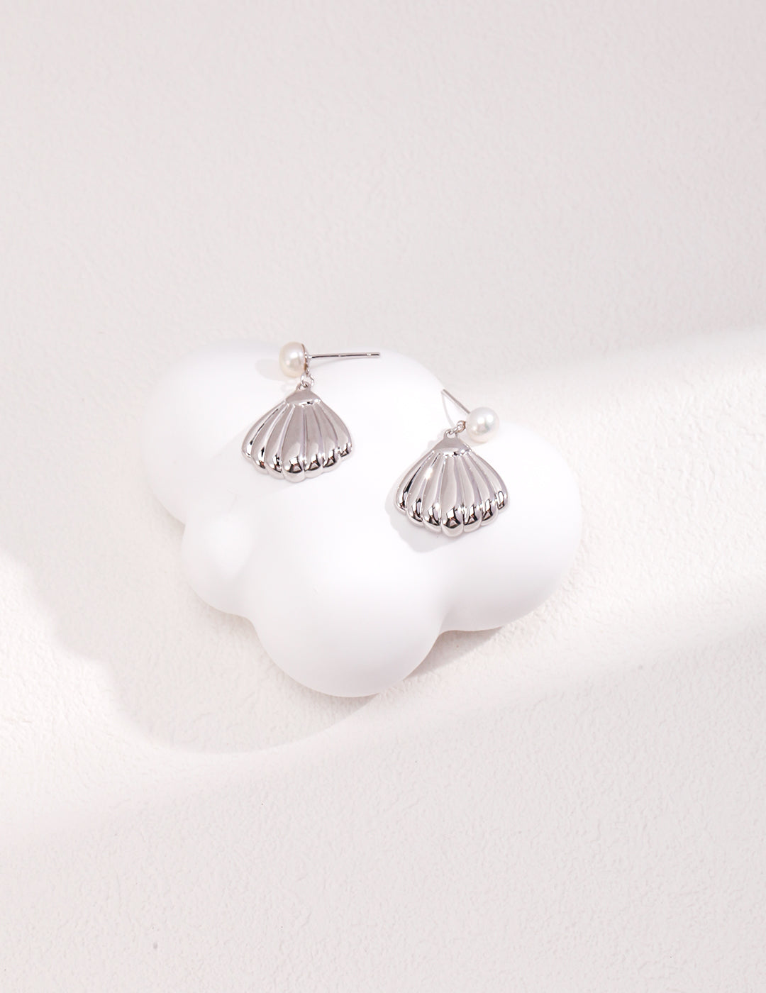 A pair of elegant silver earrings resting on a smooth white surface, showcasing their shine and intricate design.