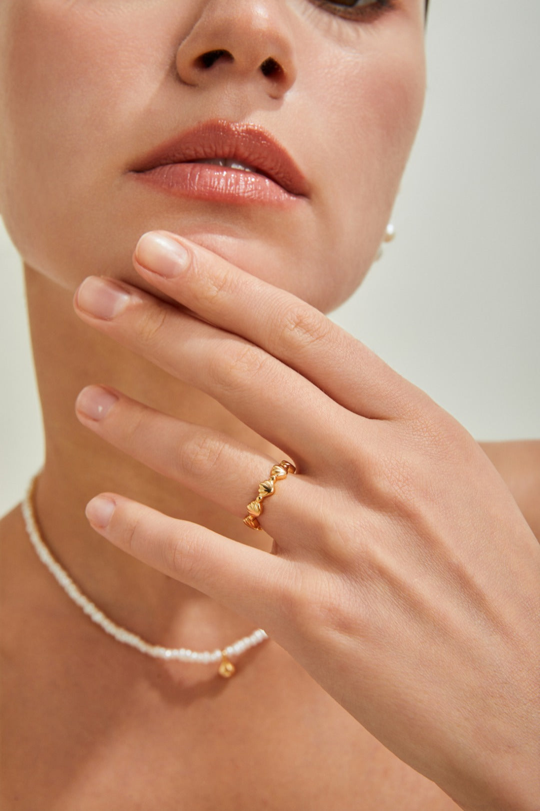 A woman adorned with a seashell-inspired gold ring and a classic pearl necklace, highlighting her refined taste in jewelry.