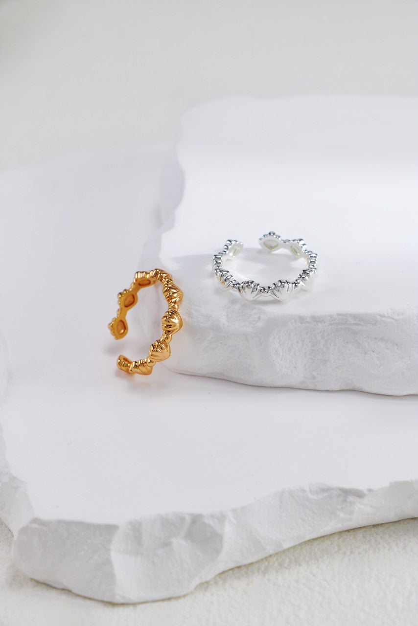 Gold and silver seashell-inspired rings elegantly placed on a white stone, emphasizing their unique craftsmanship.