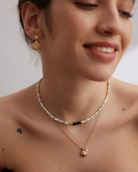 A woman displays a necklace adorned with a shell and pearl, highlighting a chic seashell-inspired jewelry look.