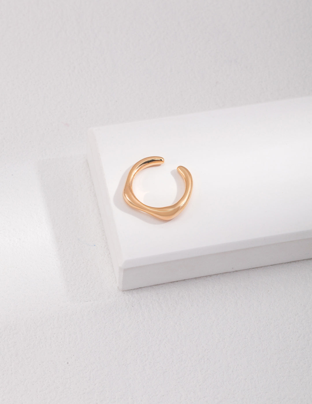 A minimalist gold ring resting on a white surface, exuding elegance and simplicity.