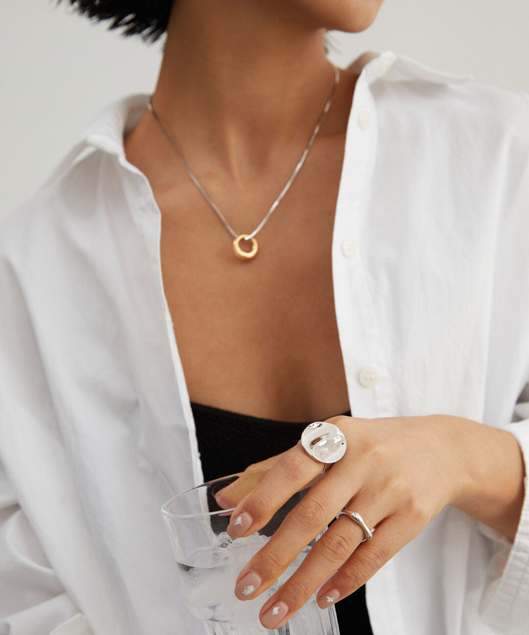 A woman in a white shirt wearing a silver minimalist ring and a silver statement ring.