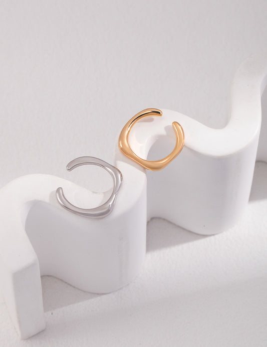 Two minimalist rings, one silver and one gold, resting on a white surface.