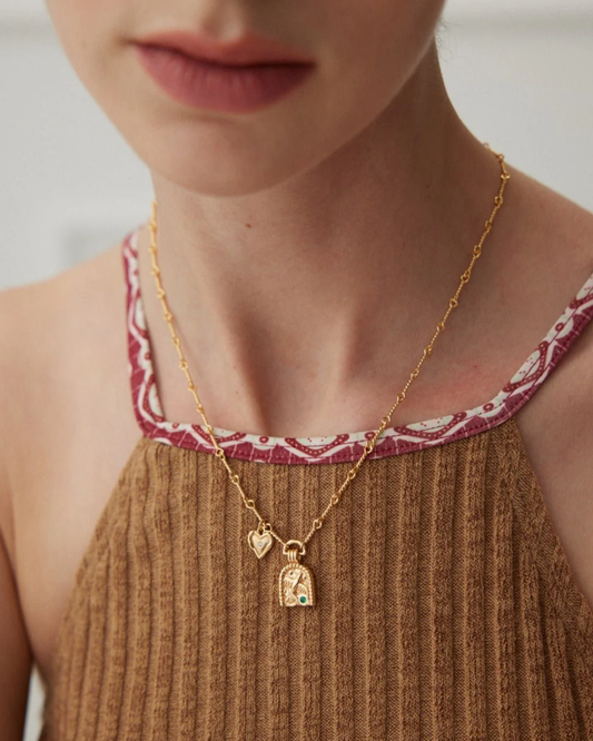 Close-up of a woman wearing a gold necklace adorned with a heart charm, highlighting her fashionable accessory.

