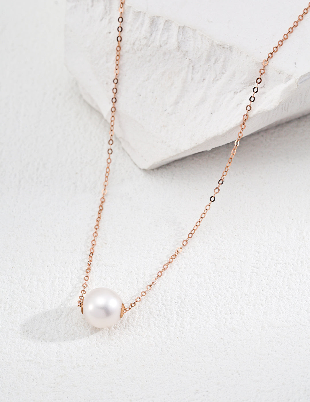 A delicate karat gold freshwater pearl necklace showcased on a clean white stone, highlighting its elegance and beauty.