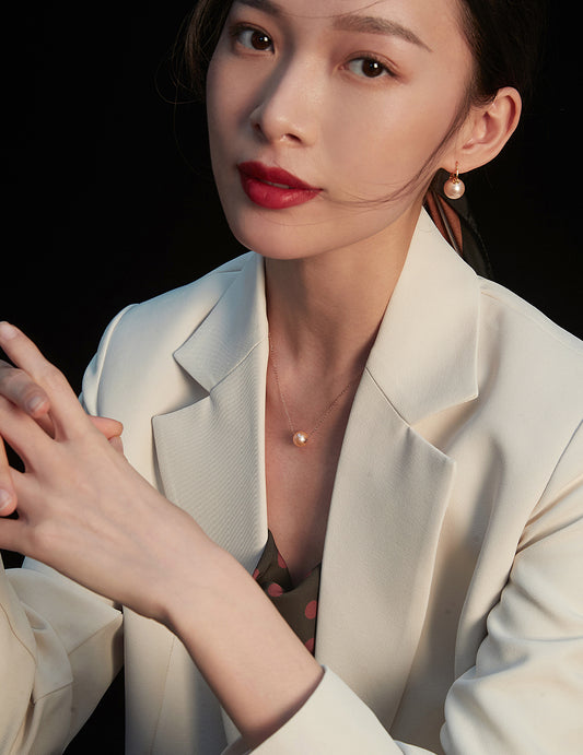  A stylish woman in a white blazer and red lipstick, adorned with a karat gold freshwater pearl necklace, radiates sophistication.