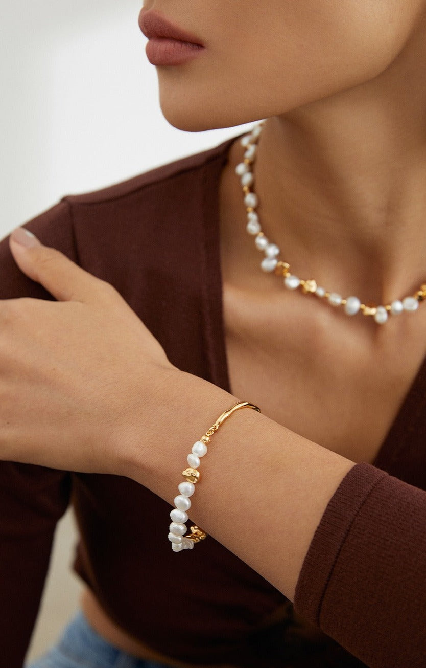 Elegant model adorned with pearls, wearing necklace and bracelet.