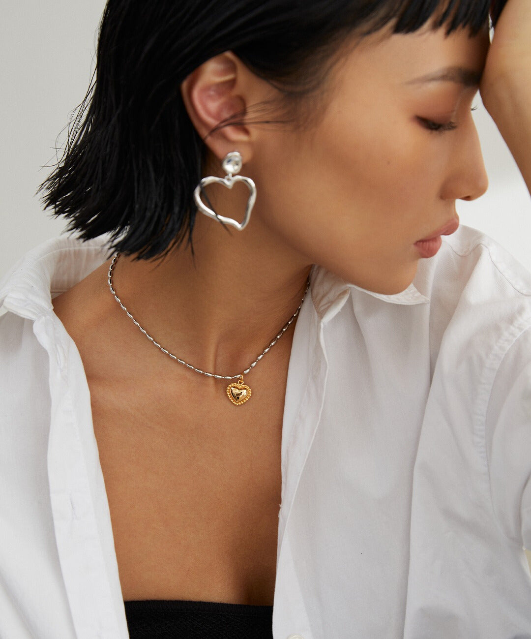 A model wearing a white shirt and a gold heart necklace with matching earrings.