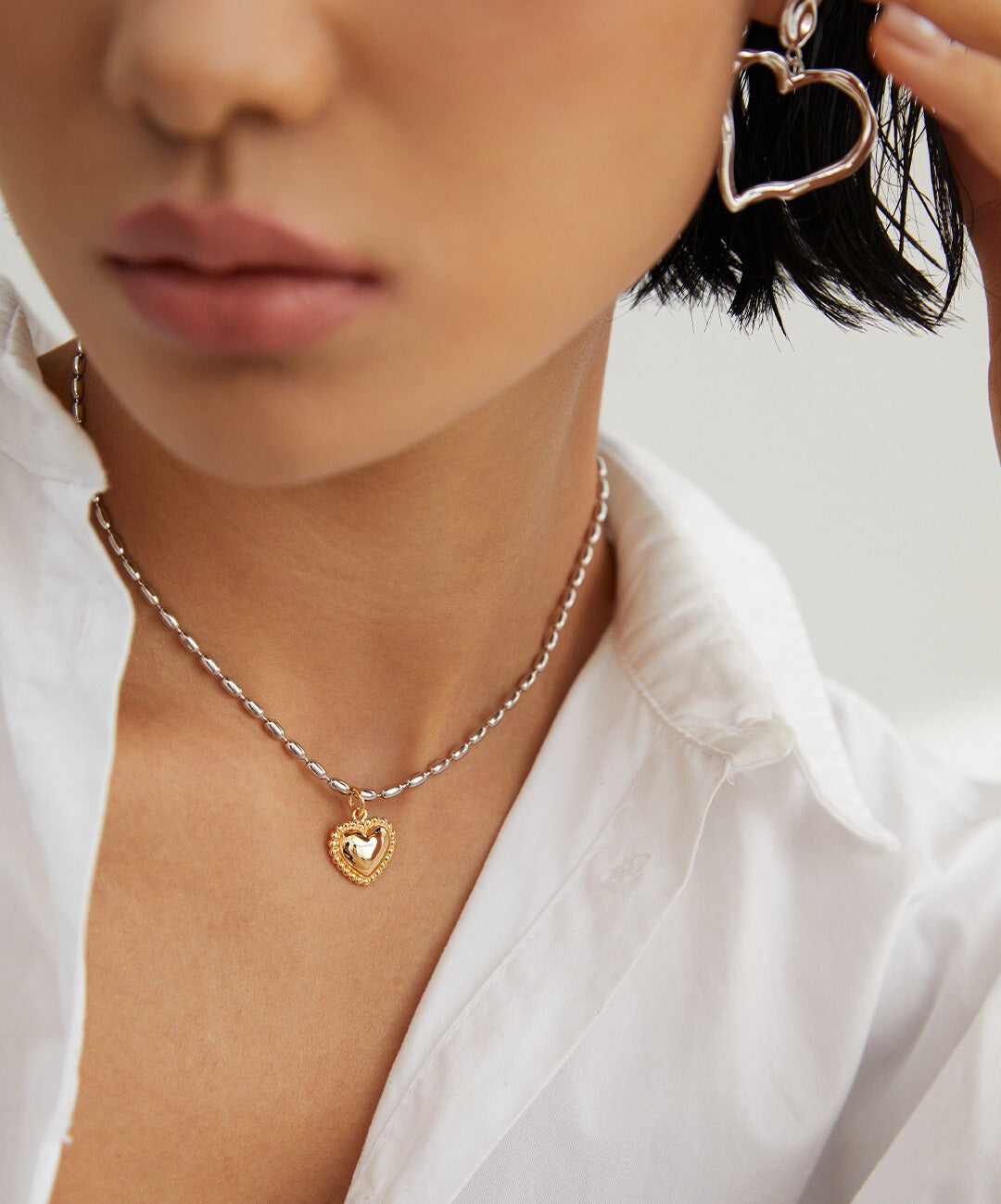 Stylish woman in white shirt accessorized with heart necklace, and matching earring.