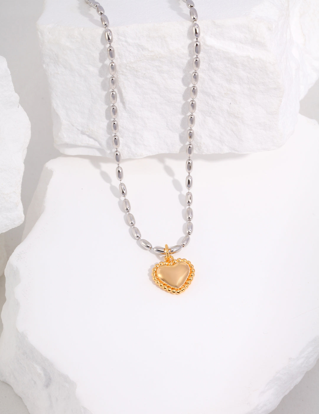 A silver beads necklace with a gold heart-shaped pendant hanging from it.