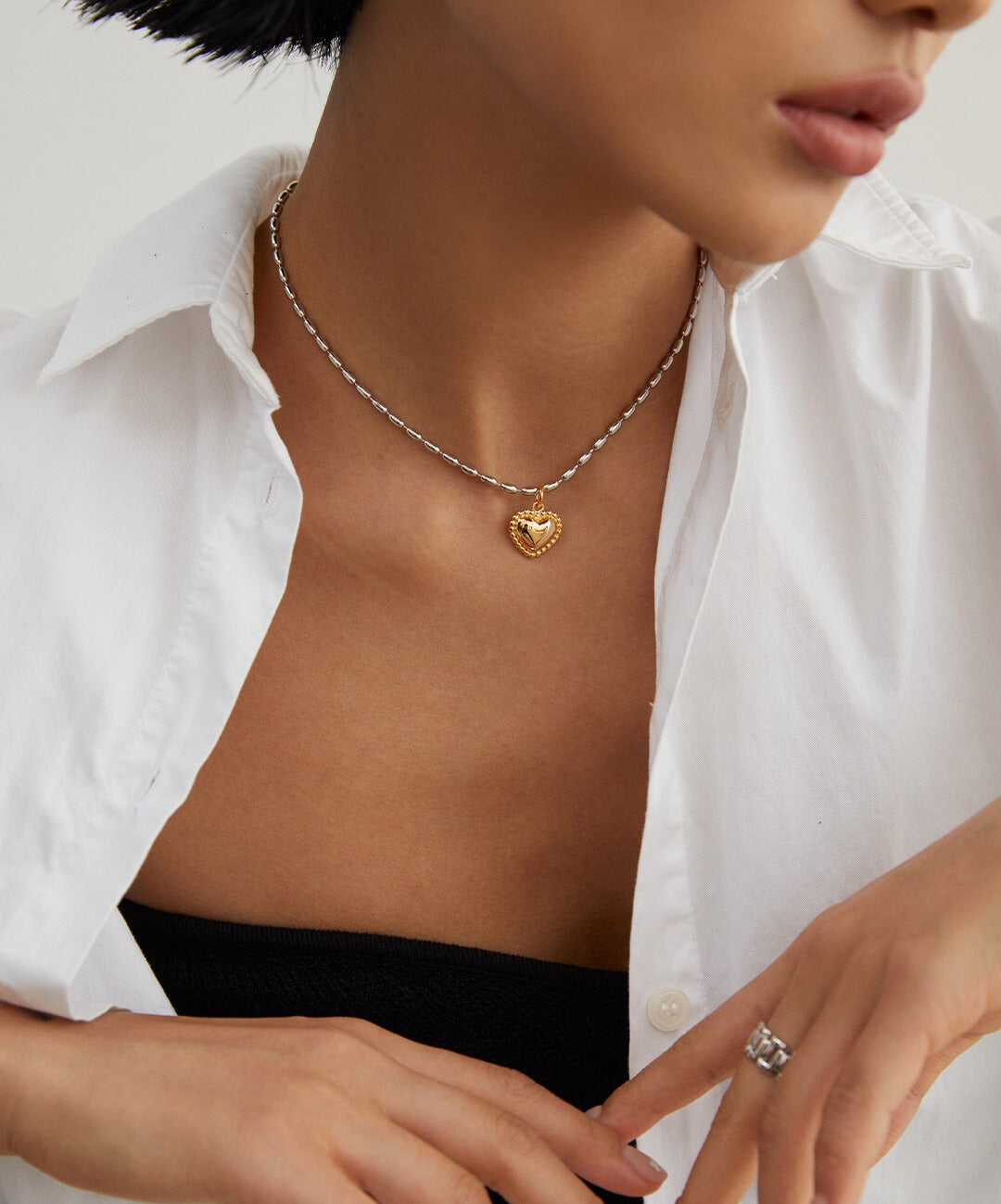 A stylish woman donning a white shirt, featuring a silver beads necklace and a charming gold heart pendant.