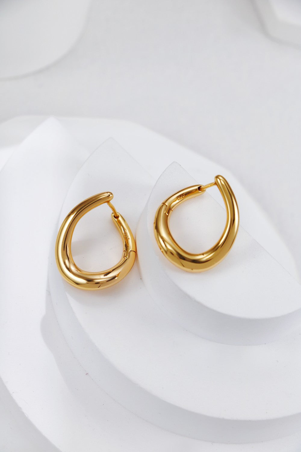 Two shiny gold hoop earrings elegantly placed on a white plate, emphasizing their beauty and craftsmanship.