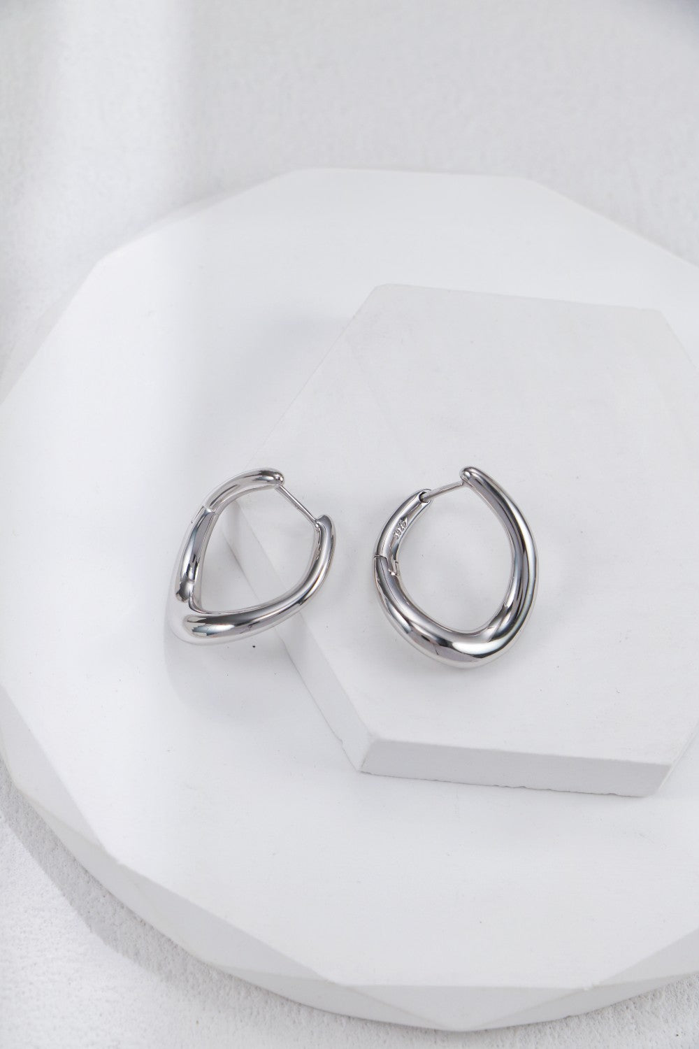 A pair of shiny silver hoop earrings resting on a clean white plate, highlighting their stylish appearance.