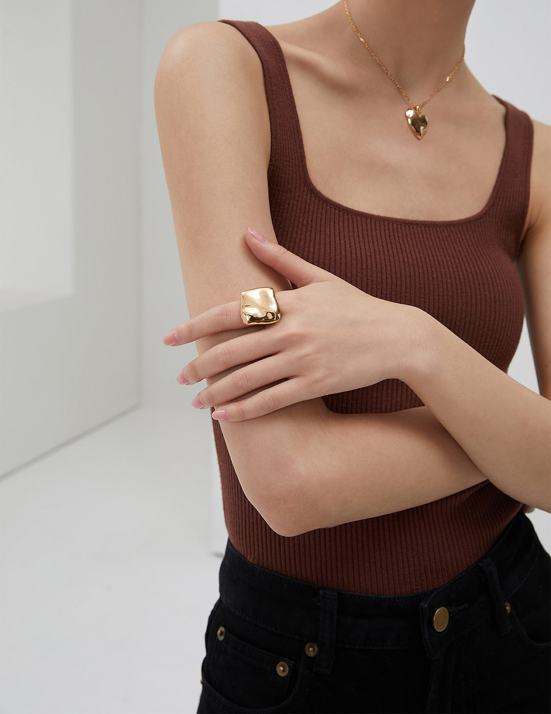 A stylish woman in a brown tank top flaunting a gold ring and other gold jewelry.