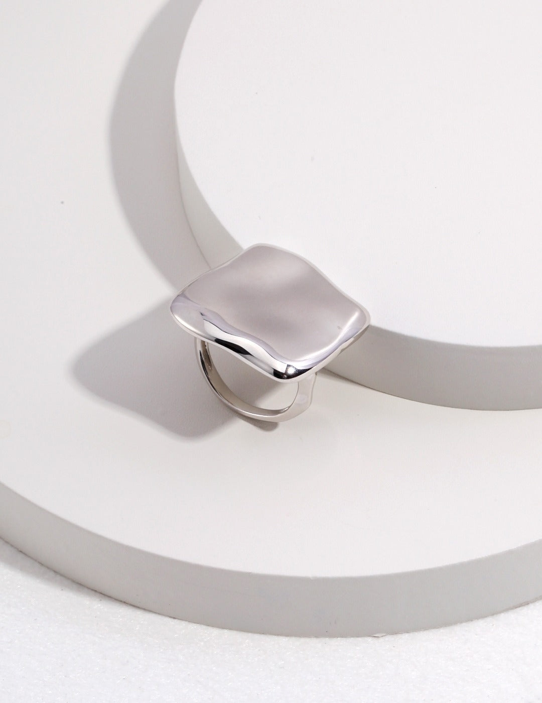 A silver squary ring resting on a white surface.