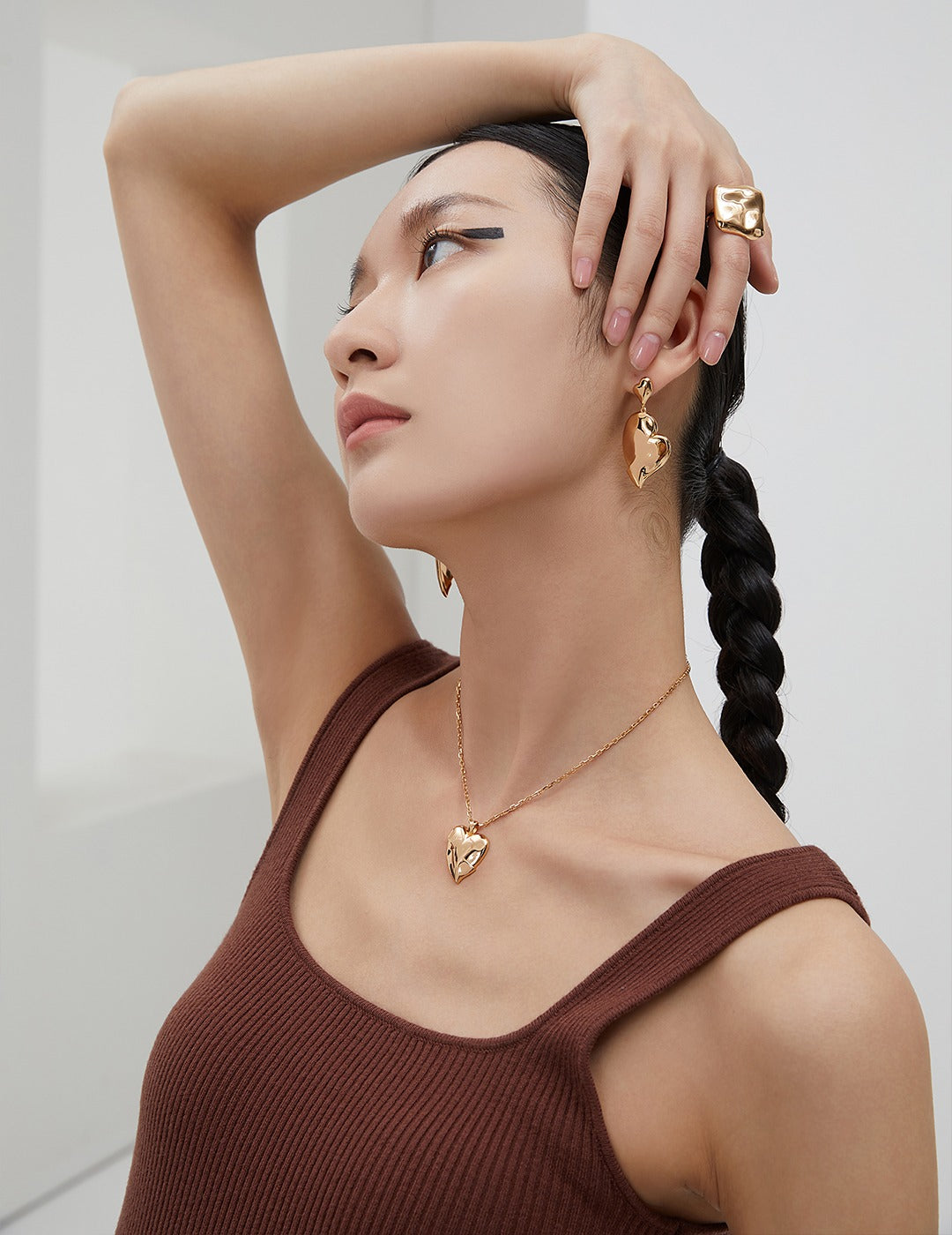 A woman in a brown top and earrings, accessorized with a gold squary ring and matching jewelry.