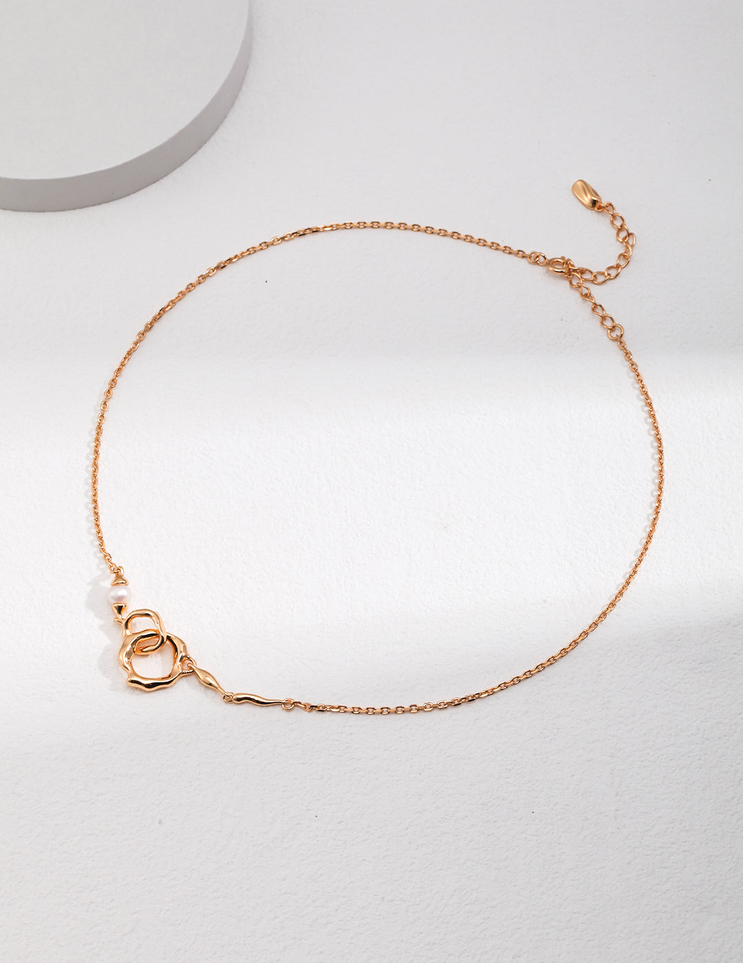 A delicate gold chain necklace adorned with interlocked gold double rings and a freshwater pearl.