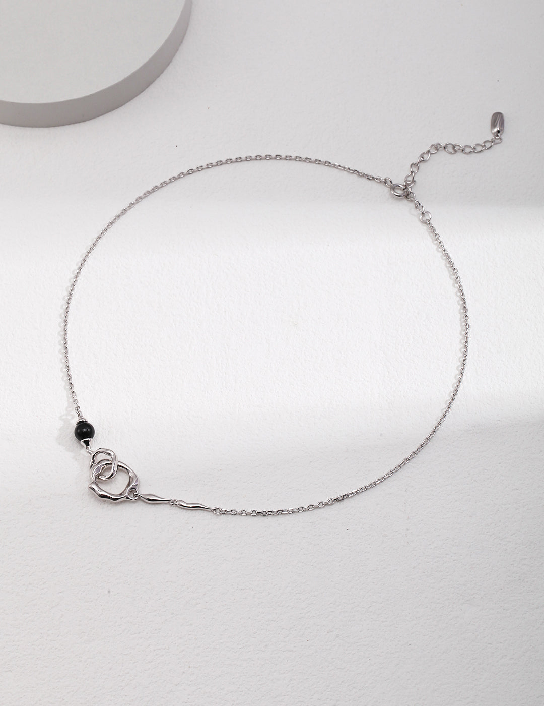 A delicate silver chain necklace adorned with interlocked gold double rings and a black agate.