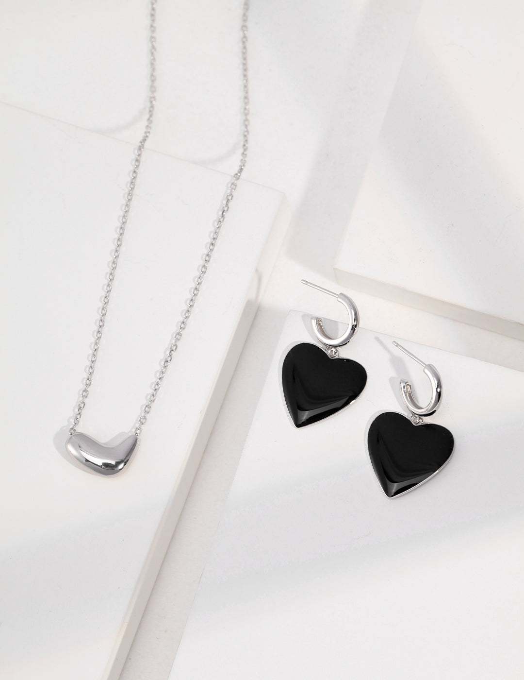 Black heart necklace and earrings set on white surface, featuring silver bean pendant necklace.