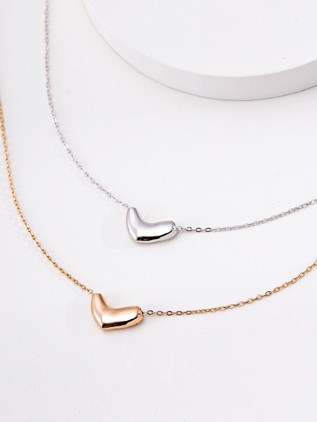 Close-up shot of the gold and silver Beanie Necklaces resting on a clean white surface, showcasing their sleek pendants.