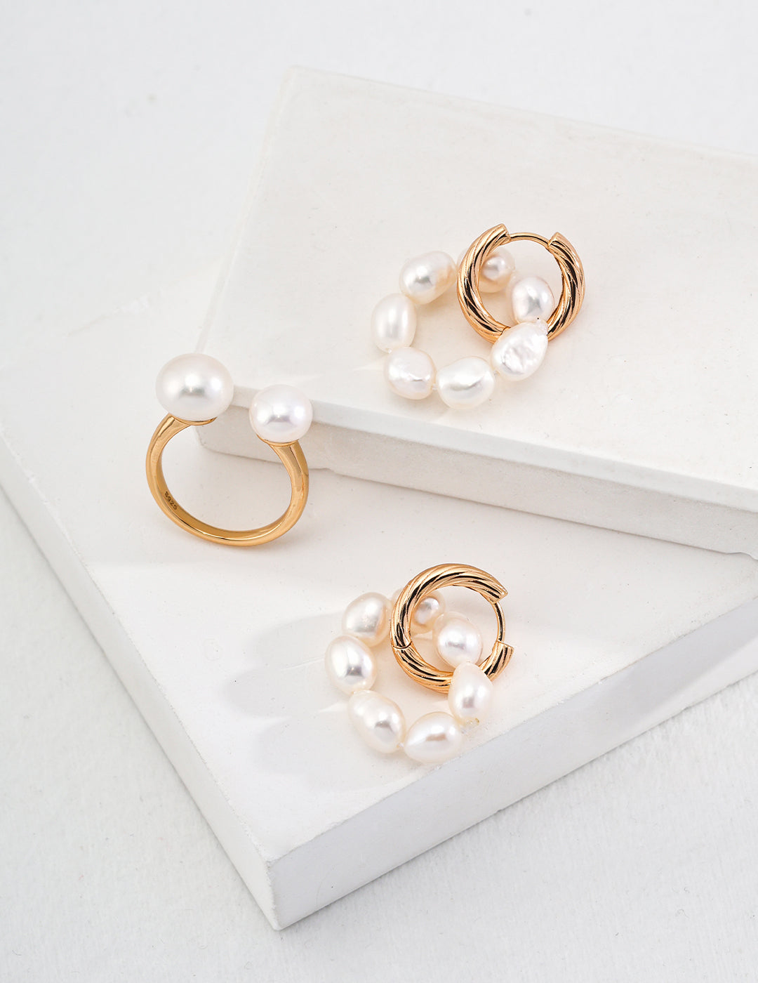 Two freshwater pearl earrings and a gold ring on a white surface, showcasing elegant and timeless jewelry.