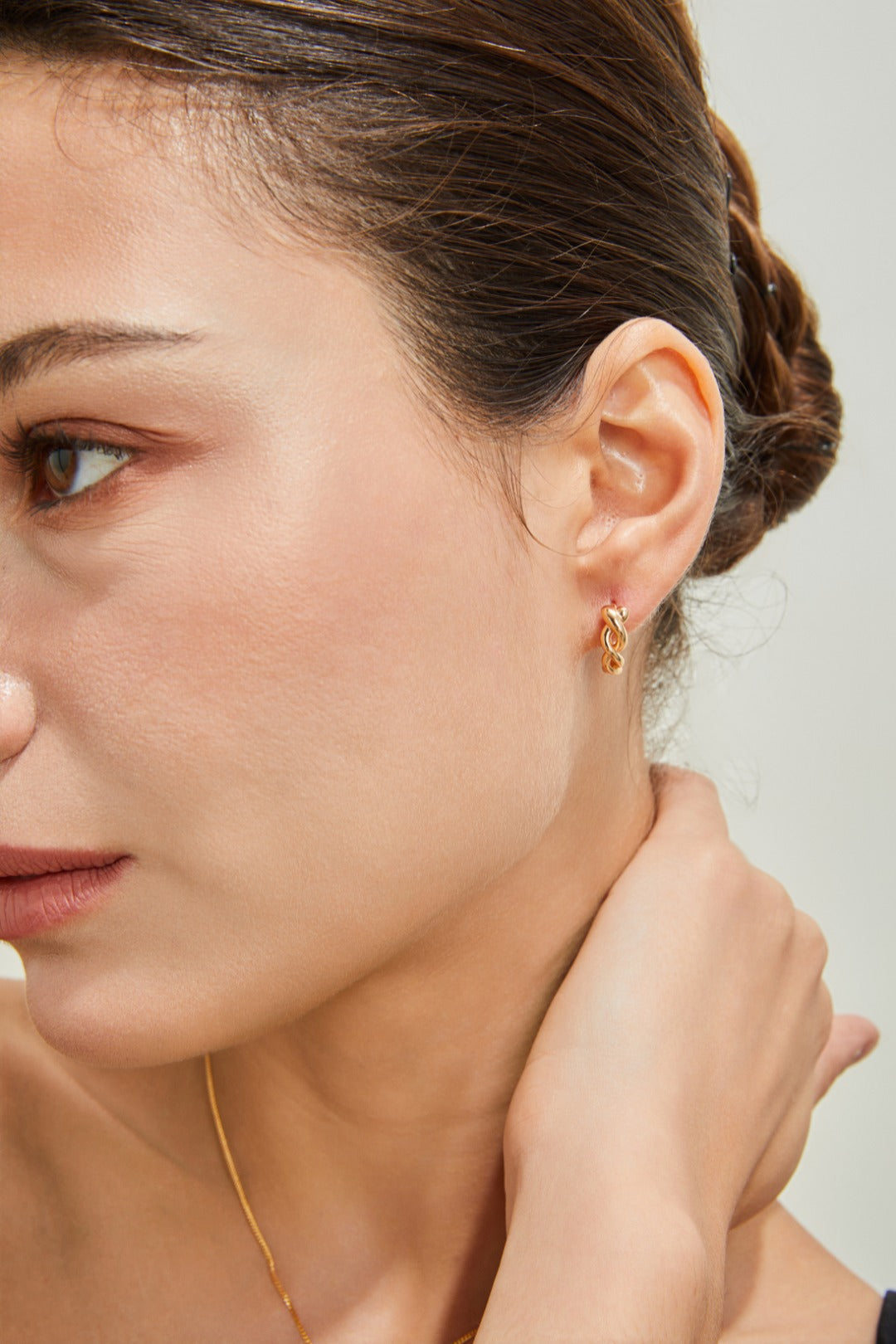 A woman poses with a gold necklace and twisted hoop earrings, emphasizing her fashionable look and elegant jewelry choice.