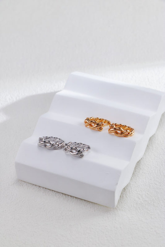 Two pairs of twisted hoops, one in gold and the other in silver, rest on a pristine white tray, emphasizing their stylish allure.