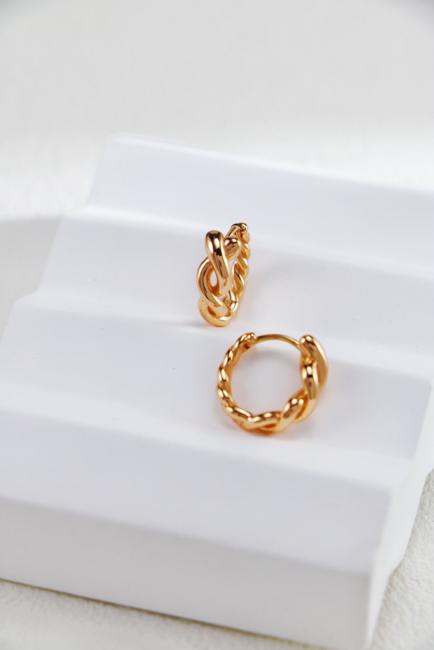 A pair of gold-plated hoop earrings resting on a pristine white background.
