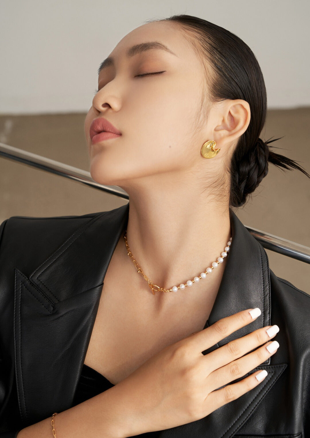 A stylish woman in a black leather jacket, showcasing a unique gold necklace with half pearls and half gold chain design.