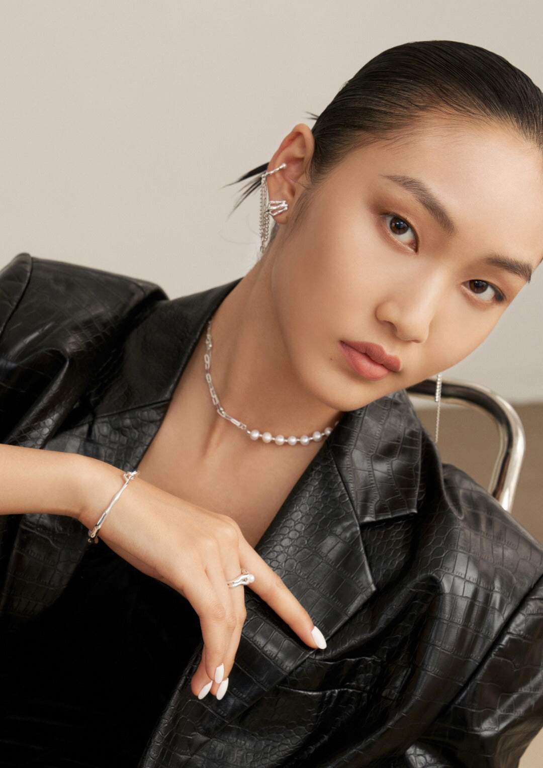 A stylish woman in a black jacket and jewelry, including a silver necklace with half pearls and half chain design.