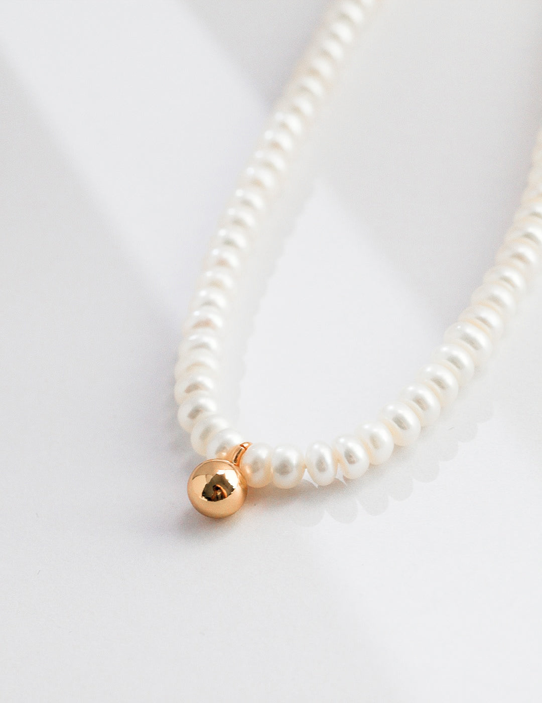 A delicate pearl necklace featuring a gold ball, elegantly displayed on a smooth white surface.