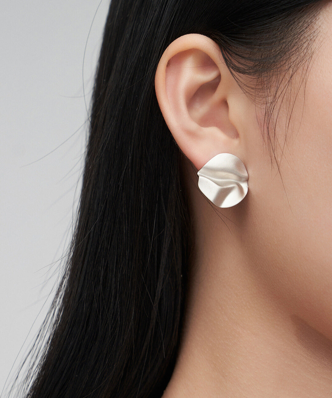 Woman wearing silver wavy stud earrings with leaf design.