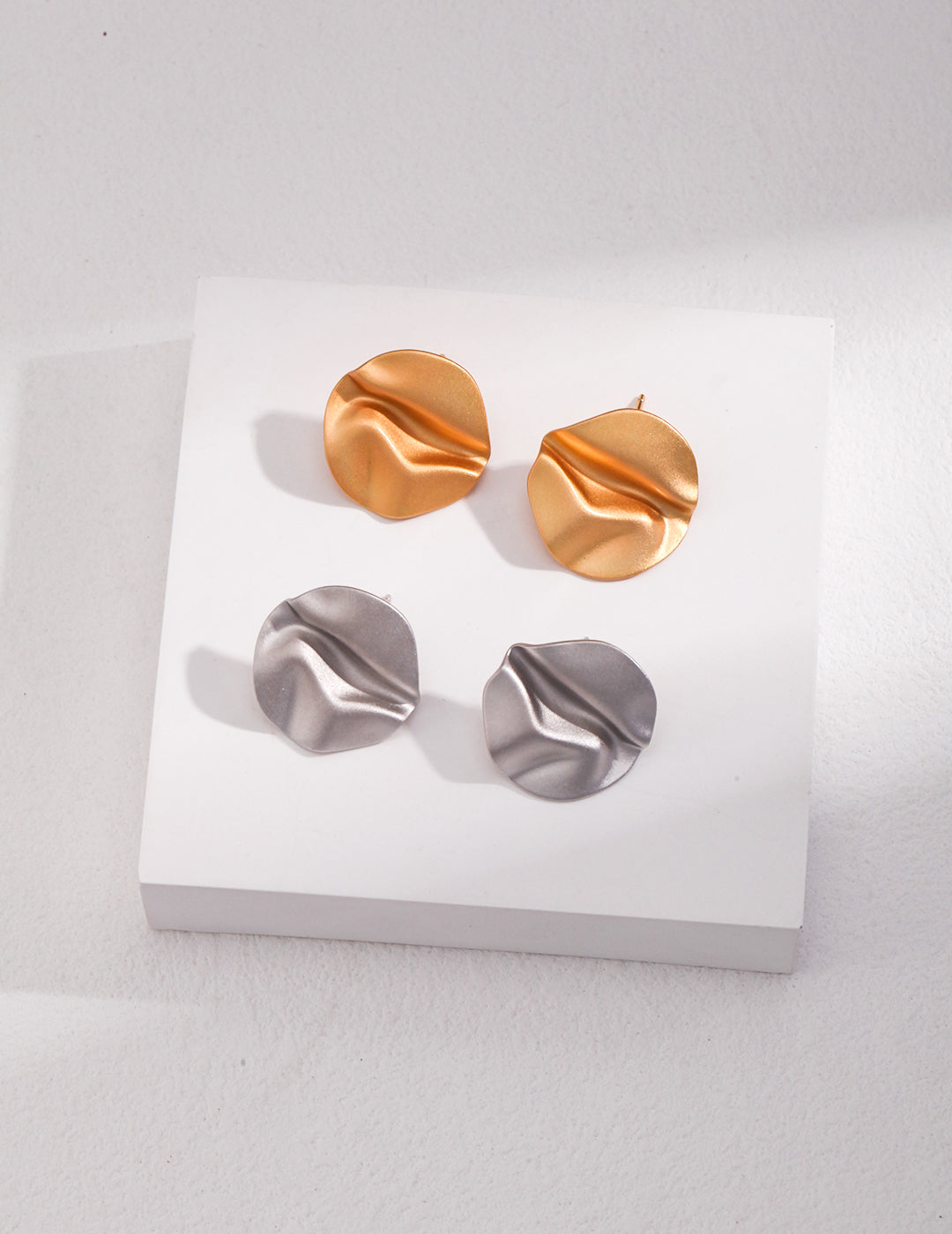 Two pairs of gold and silver earrings on a white surface - silver and gold wavy striking studs.