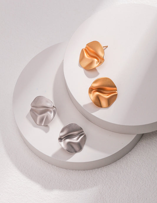 Vibrant earrings in silver and gold, with wavy striking studs, arranged on a white surface.