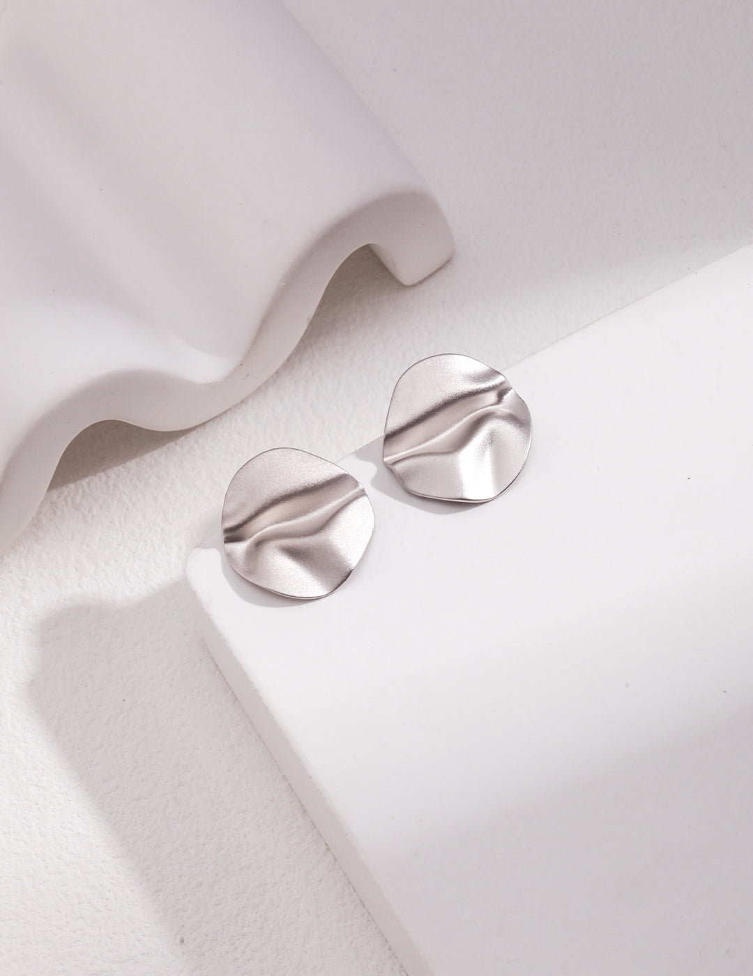 A stunning pair of silver earrings with a wavy design, resting on a pristine white surface.