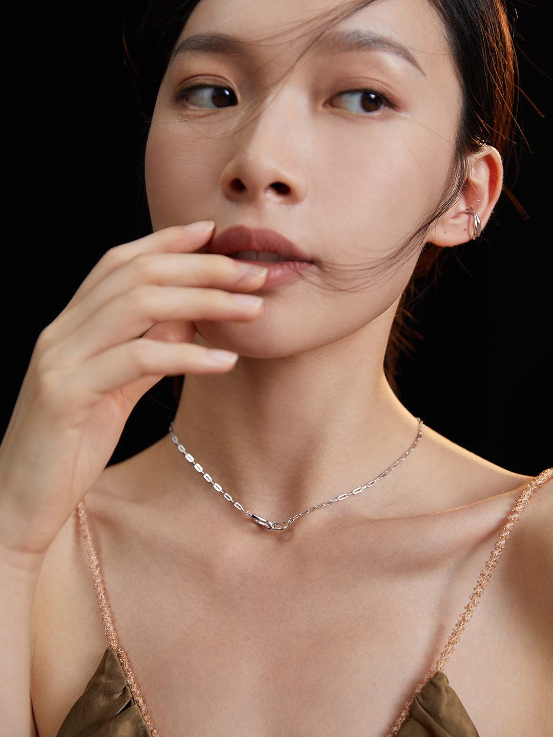 A woman wearing a silver chain necklace with an interlocked ring charm.