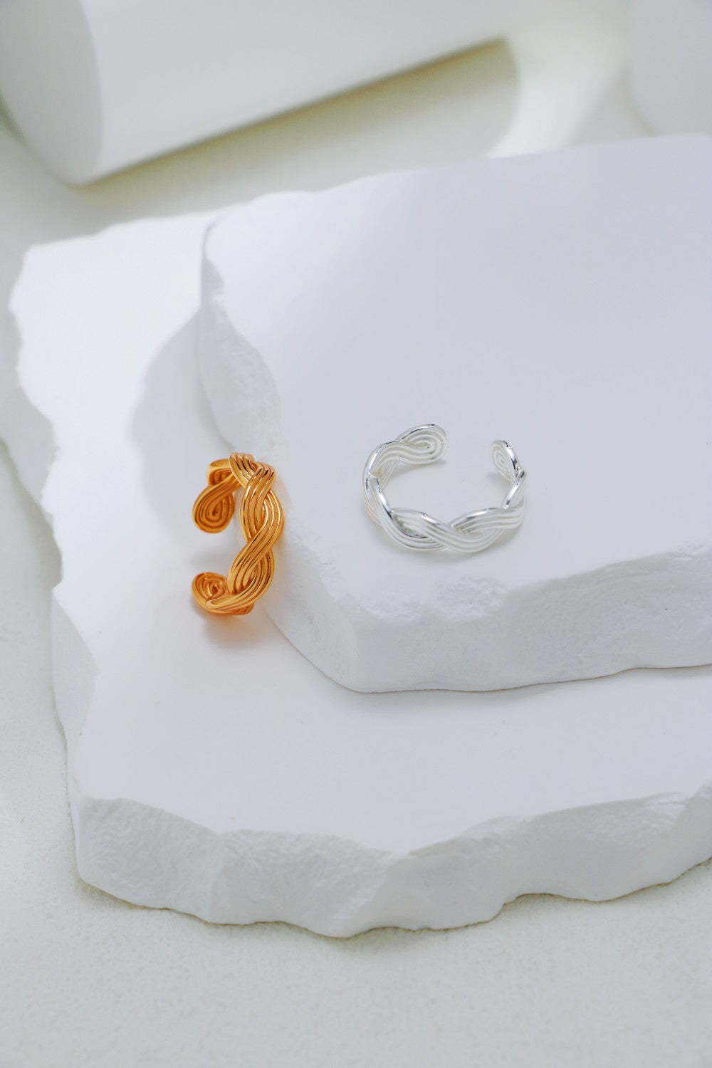 Two stylish braided rings, one silver and one gold, placed on a clean white surface.
