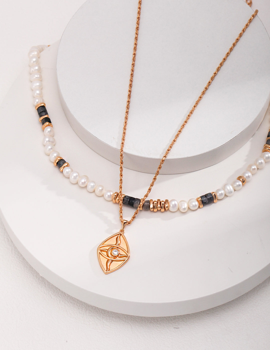 A gold plated pendant necklace layered with a pearl necklace, creating an elegant and stylish accessory.