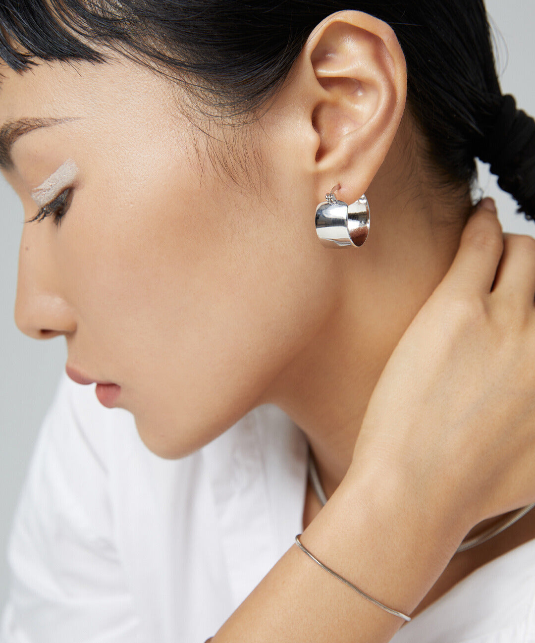 Stylish woman in white shirt accessorized with silver chunky hoops earring.