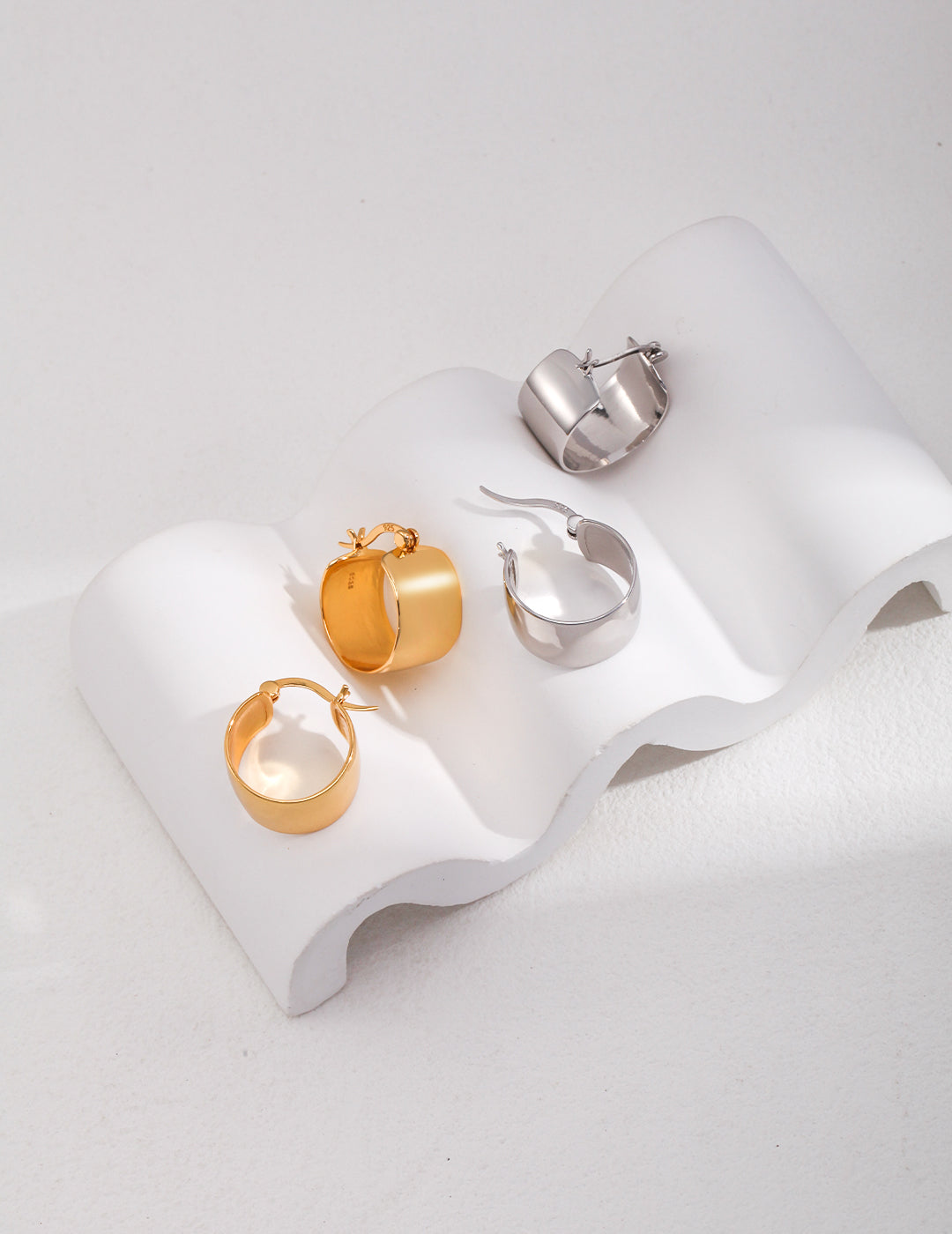 Gold and silver chunky hoop earrings arranged in pairs on a white surface.