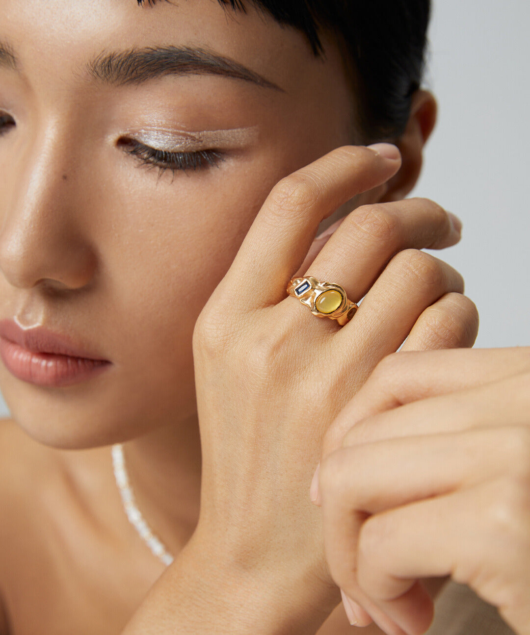 Stylish woman showcasing gold and pearl jewelry, featuring a gold open ring with colored cubic zirconia stones.