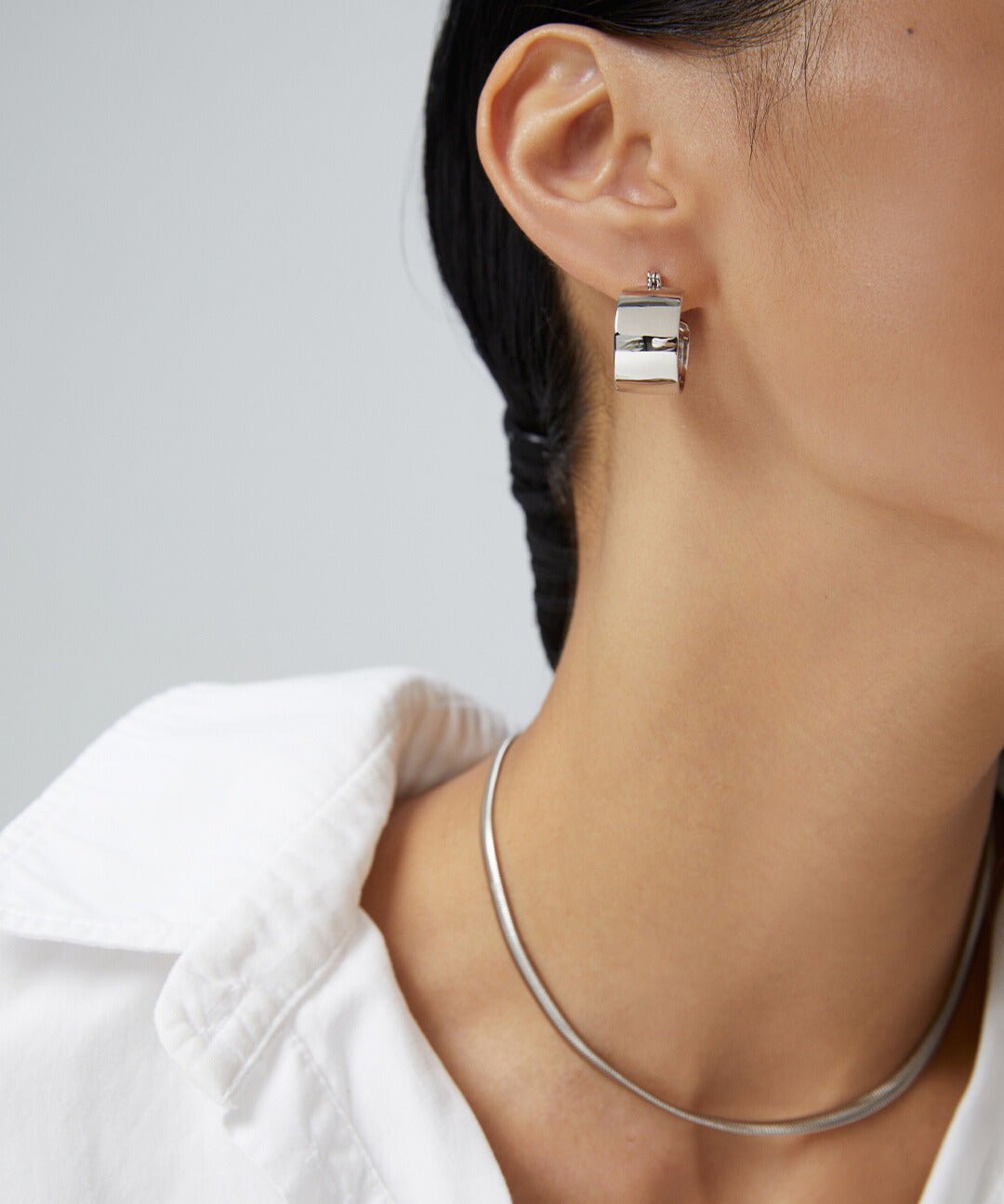 A model wearing a white shirt and silver chunky hoops earrings.