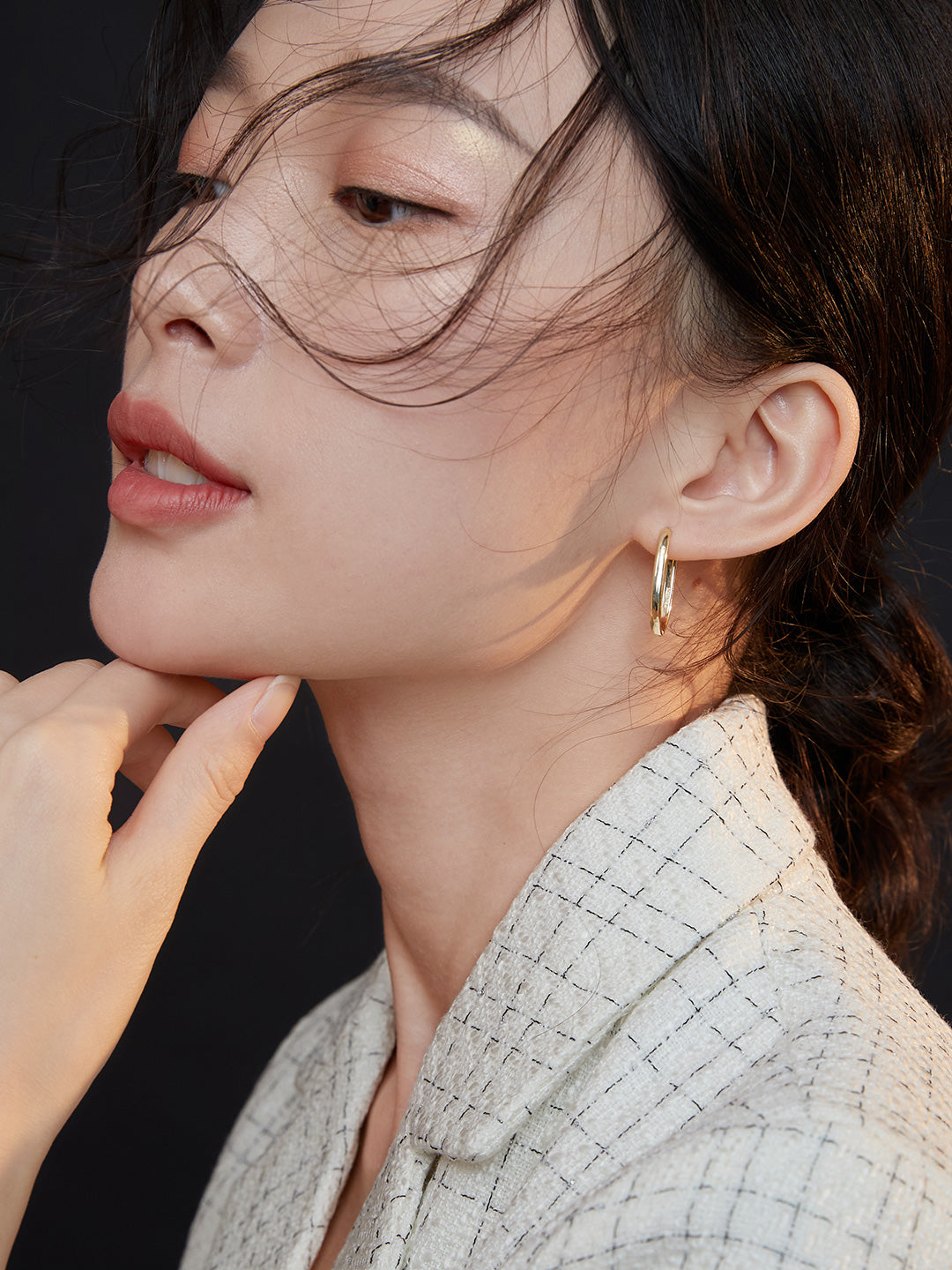 A model wearing a gold hoop earring, deep in thought with her hand resting on her chin.